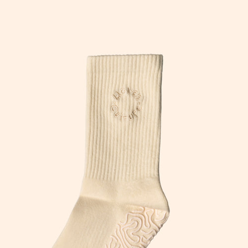 Close-up of Woven Culture cream organic grip sock with ribbed ankle and embroidered circular logo.